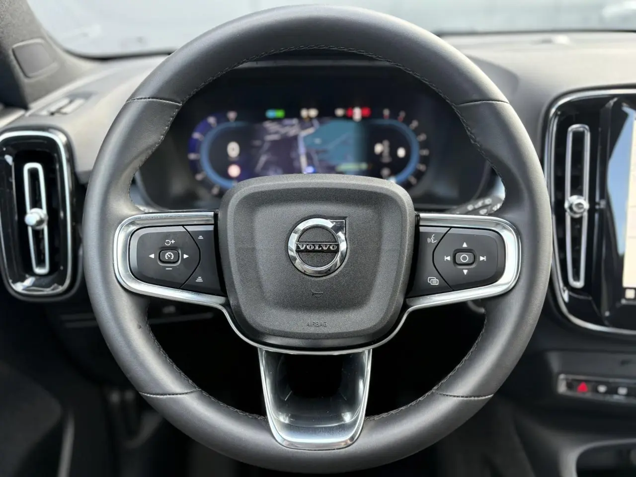 Volant cuir noir de Volvo XC40 2024 avec commandes intégrées et tableau de bord digital en arrière-plan.