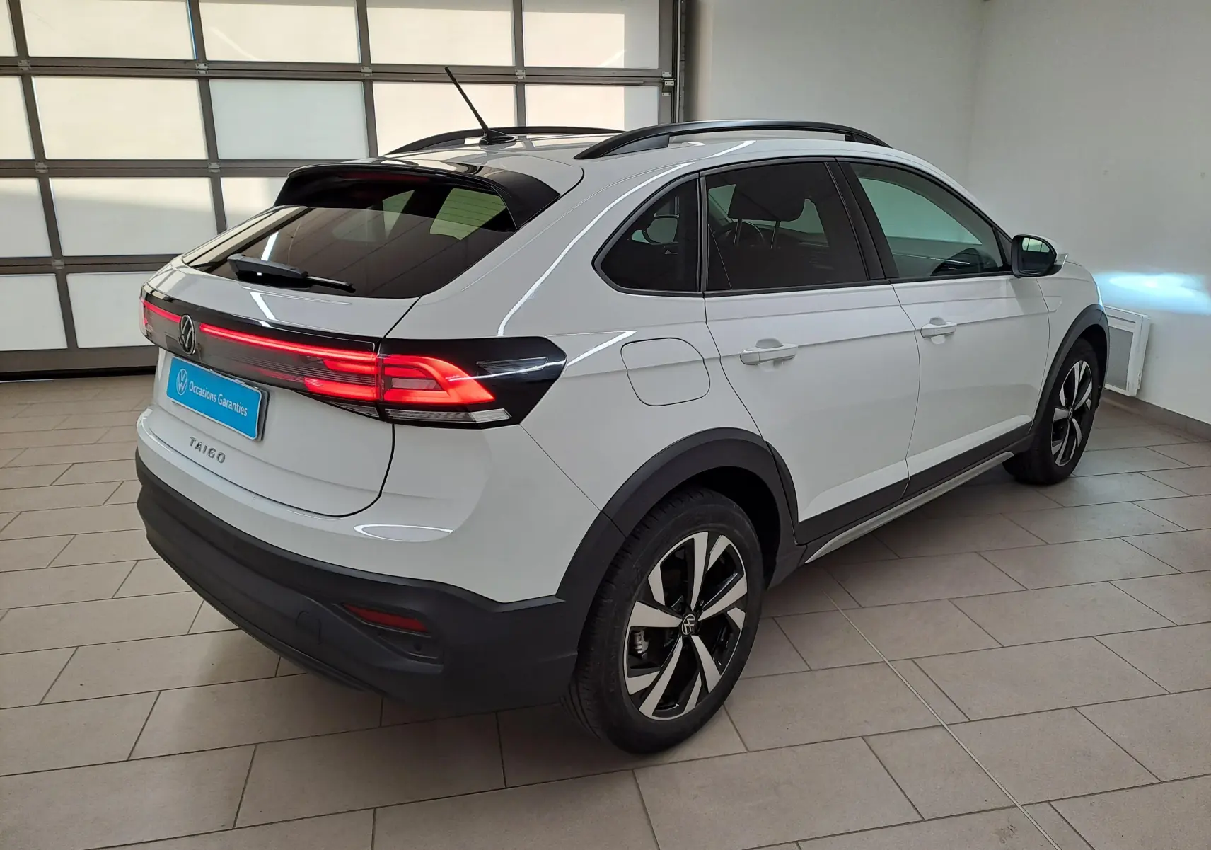 Vue 3/4 arrière droite d'un Volkswagen Taigo blanc pur 2024 avec jantes alliage Aberdeen et feux arrière LED allumés.