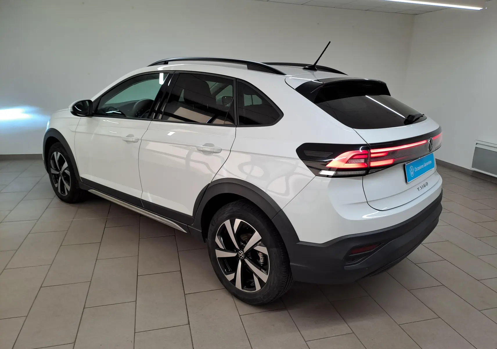 Volkswagen Taigo blanc pur vue 3/4 arrière droit, jantes alliage 17 pouces et feux arrière LED allumés.