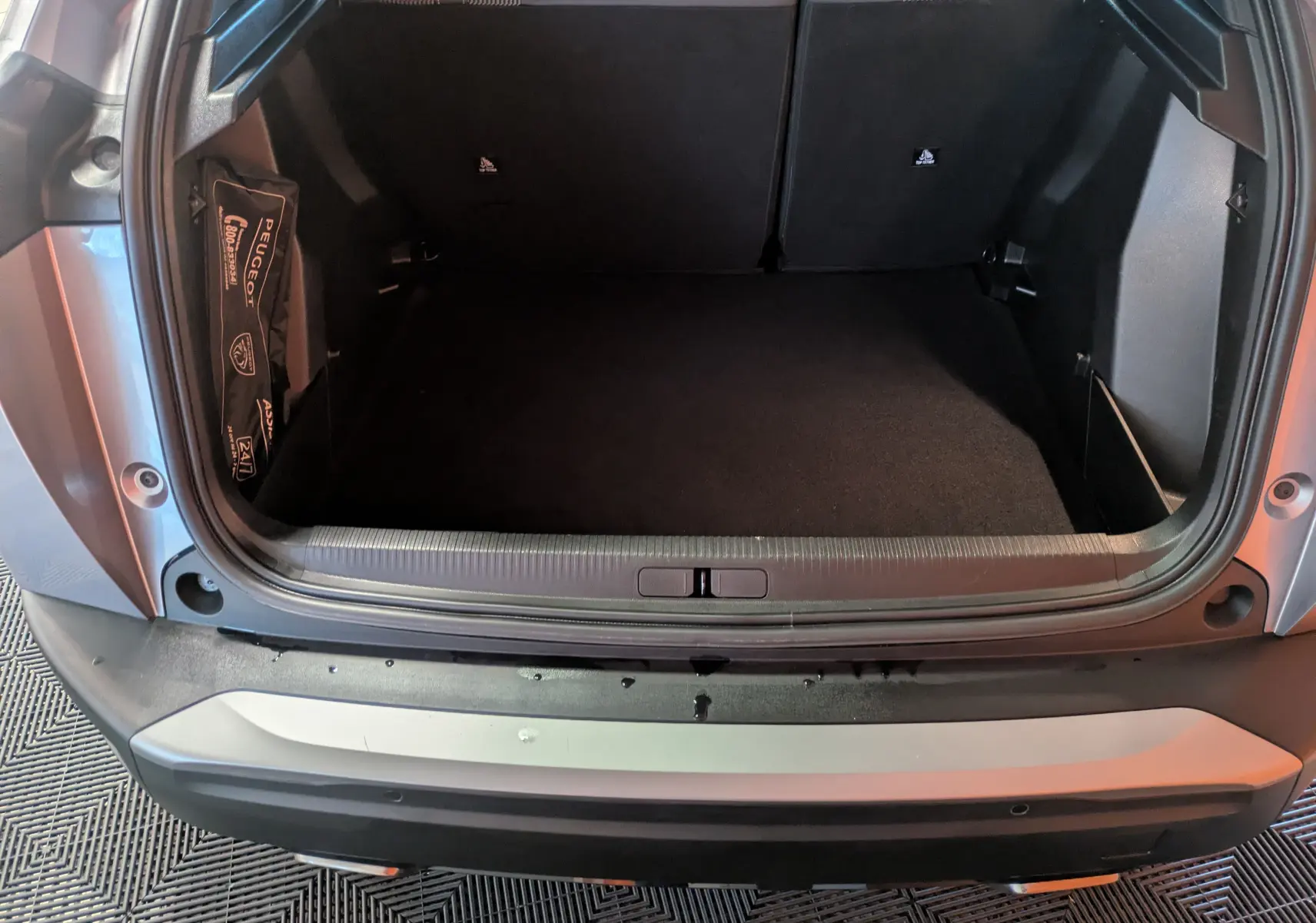 Coffre ouvert vu de l'arrière d'un Peugeot 2008 Hybrid 145 gris Artense avec toit noir, montrant l'espace de chargement vide.