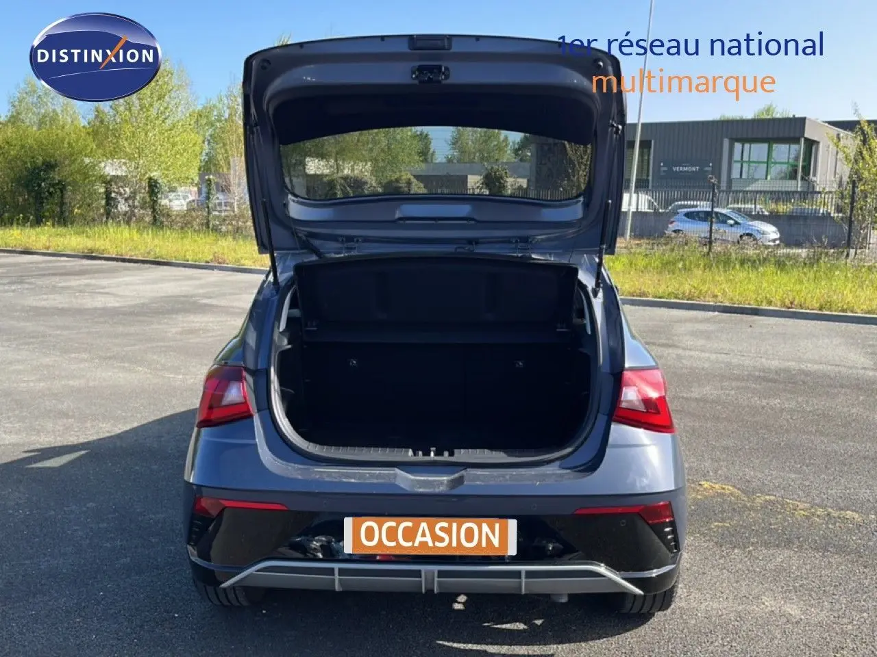 Vue arrière d'une Hyundai i20 gris aurora métal 2025 avec le coffre ouvert sur un parking extérieur.