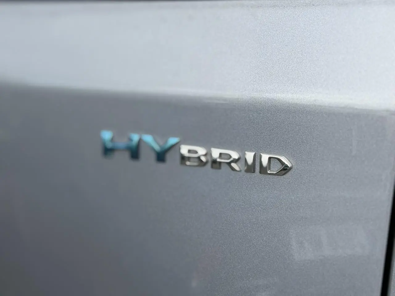 Gros plan sur le badge HYBRID bleu et chrome sur la porte arrière grise Artense d'un Peugeot 3008.