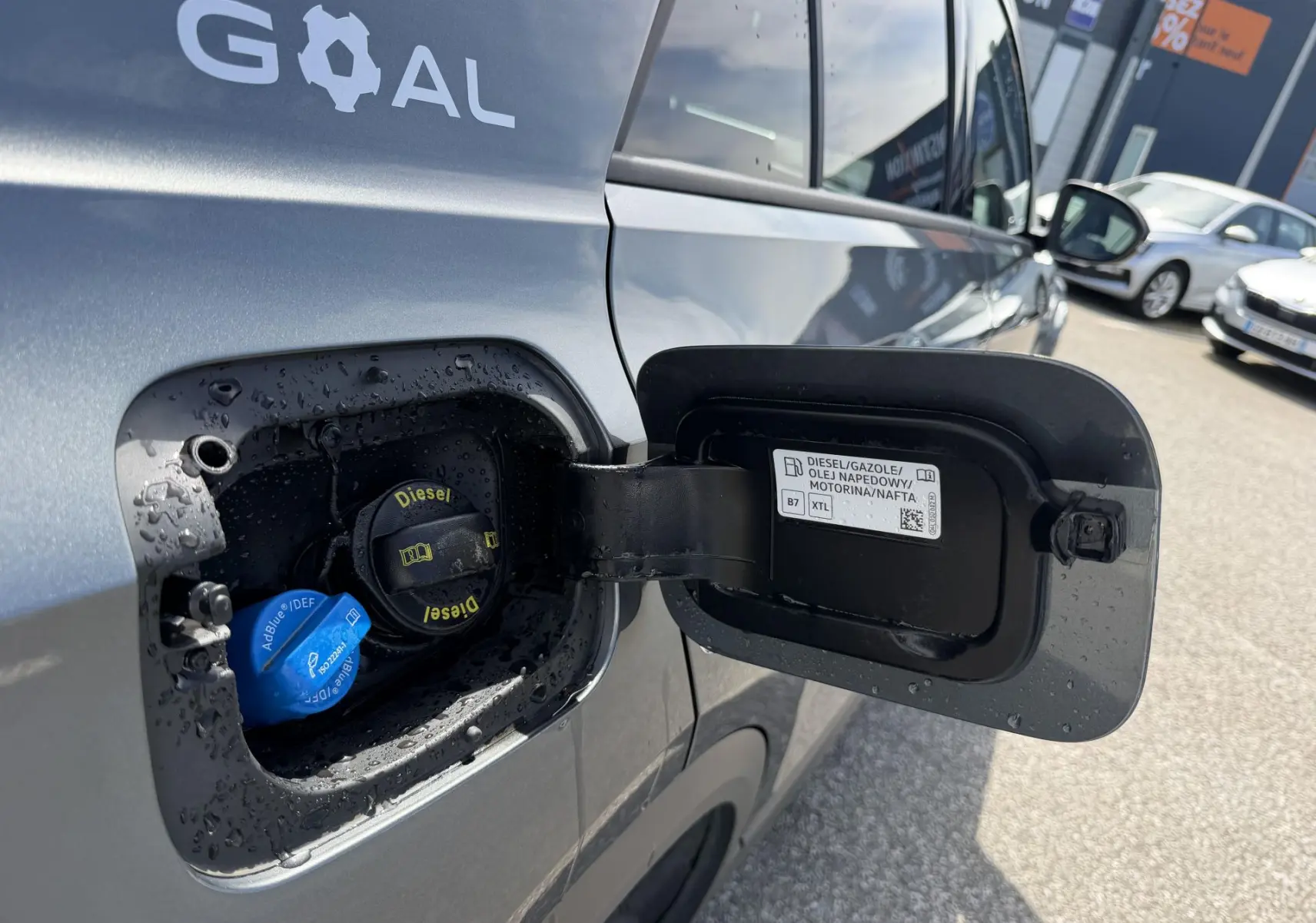 Vue rapprochée du côté gauche sur la trappe de carburant ouverte d’un Volkswagen T-Roc gris avec bouchons Diesel et AdBlue visibles.