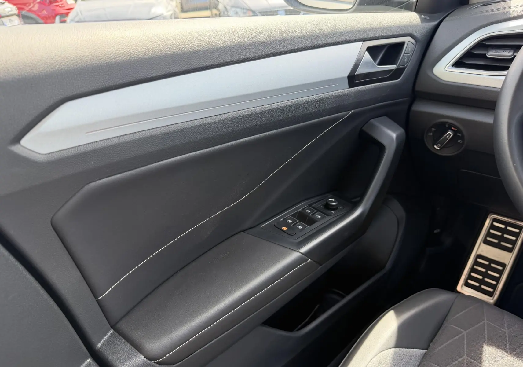 Vue intérieure côté conducteur du Volkswagen T-Roc 2025, montrant la portière noire avec surpiqûres blanches et commandes électriques.