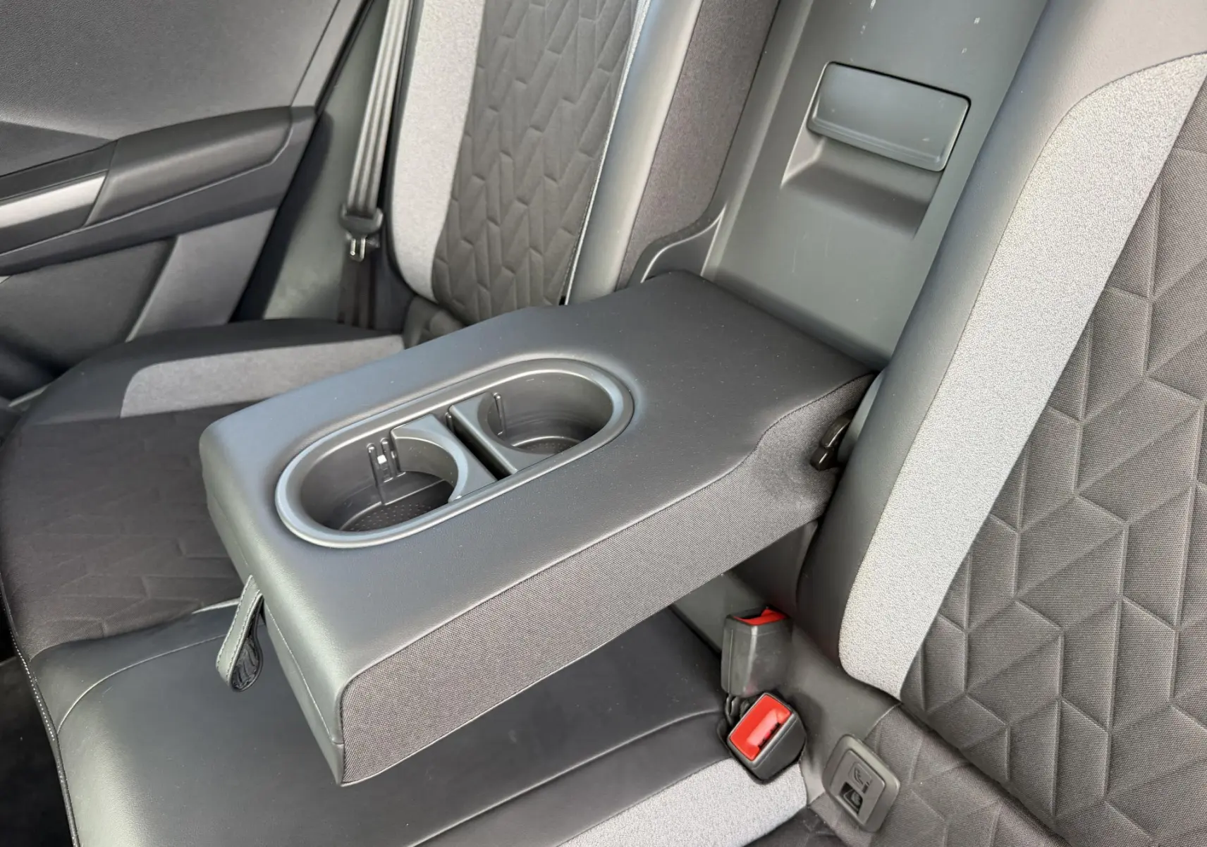 Vue rapprochée de l'accoudoir central arrière avec porte-gobelets sur les sièges bicolores gris du Volkswagen T-Roc 2025.