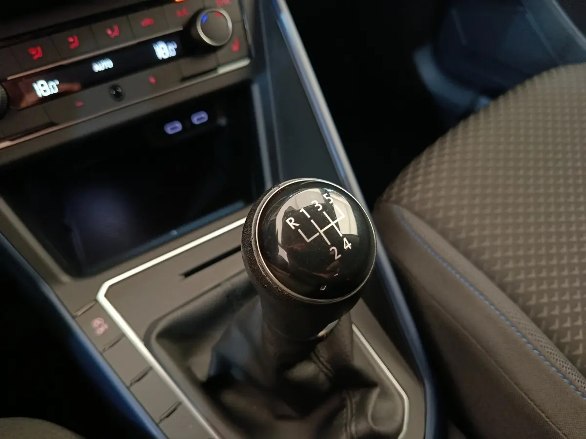 Gros plan sur le levier de vitesses manuel noir dans l’habitacle sombre de la Volkswagen Polo orange, siège tissu visible.