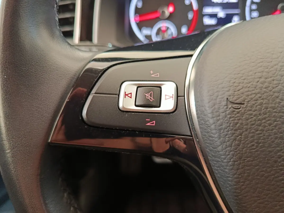 Gros plan sur les commandes du volant cuir et alu de la Volkswagen Polo 1.0 TSI 95 United, avec indicateurs rouges.