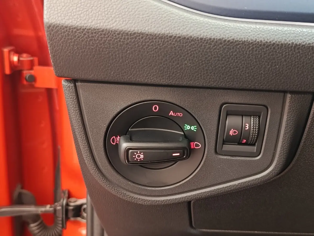Gros plan sur le bouton de commande des phares dans l'habitacle d'une Volkswagen Polo orange, côté gauche.