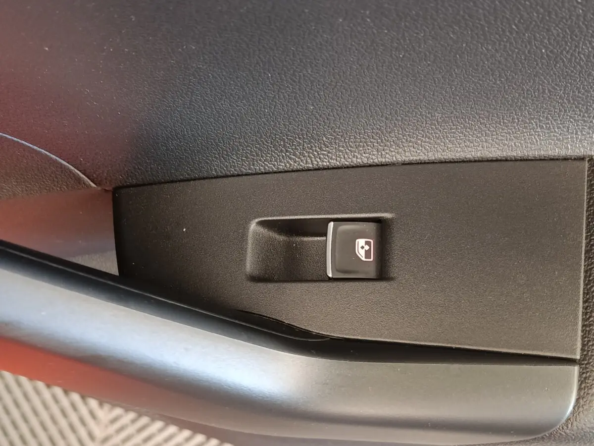 Gros plan sur le bouton de commande de la vitre électrique côté conducteur dans l'habitacle d'une Volkswagen Polo orange.