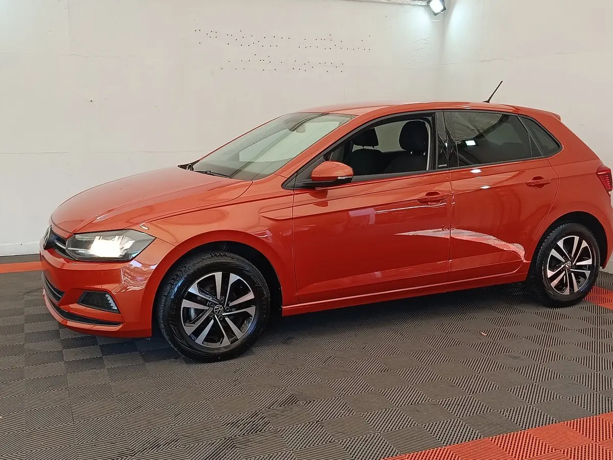 Vue de profil côté gauche d'une Volkswagen Polo orange 2020 avec jantes alliage et phares allumés.