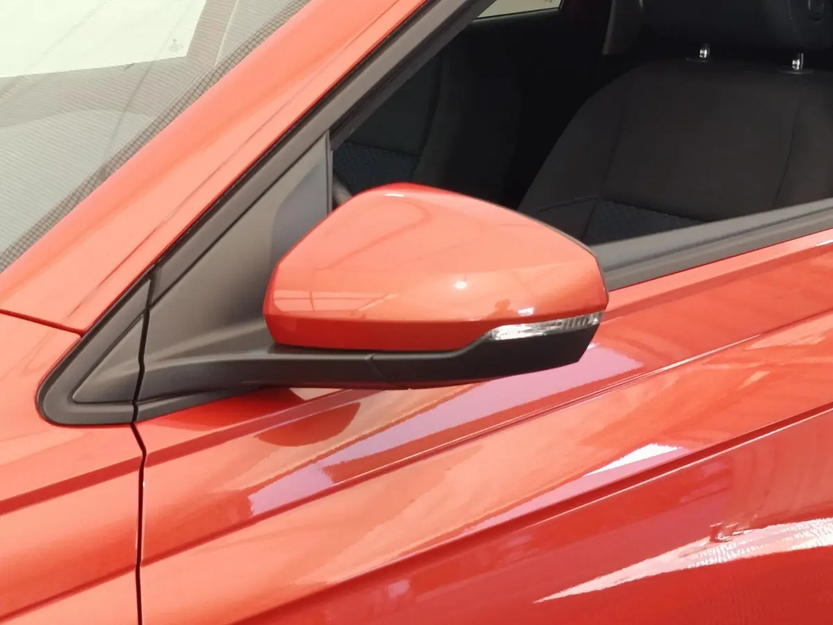 Gros plan sur le rétroviseur côté gauche d'une Volkswagen Polo orange 2020 avec portière et siège noir visibles.