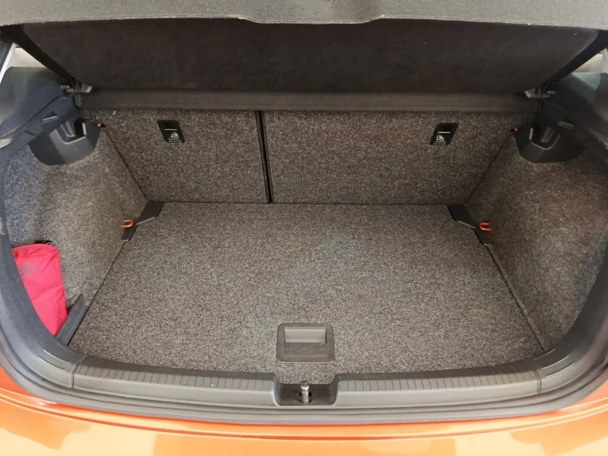 Coffre ouvert vu de face d'une Volkswagen Polo orange 2020, intérieur gris avec tapis de sol et rangement latéral.