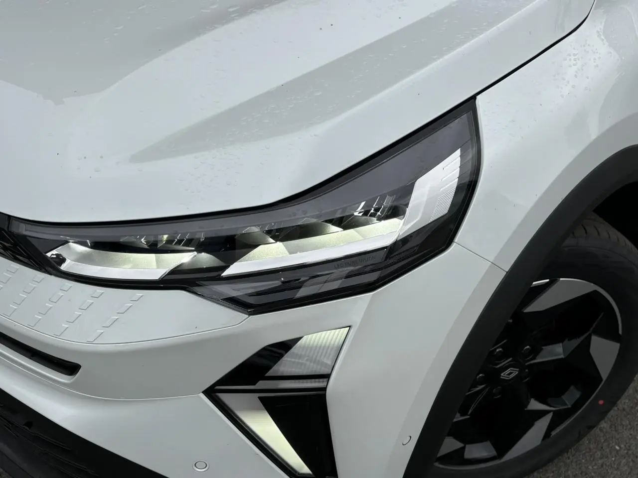 Gros plan sur l'avant droit du Renault Captur blanc nacré, mettant en valeur le phare LED et la jante aluminium noire.