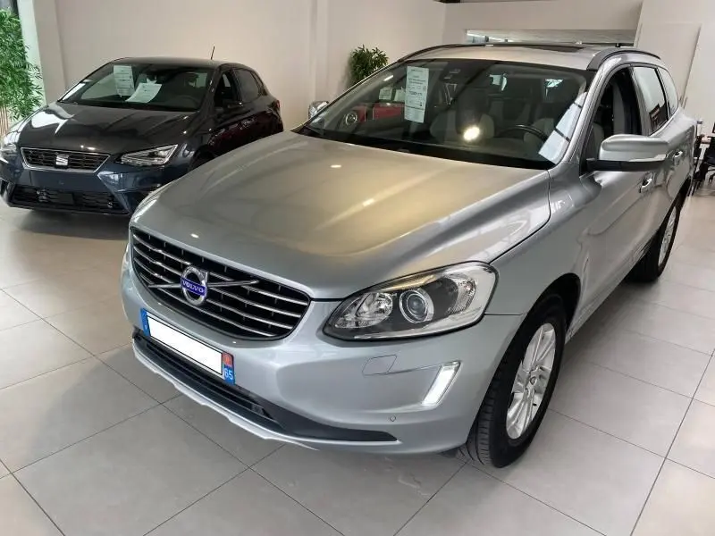 Vue 3/4 avant droite d'un Volvo XC60 argenté avec barres de toit et feux LED dans un showroom.