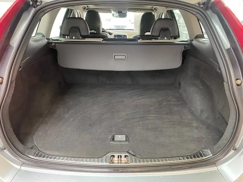 Coffre ouvert vu de l'arrière d'un Volvo XC60 argenté, montrant un espace de chargement propre avec cache-bagages déployé.