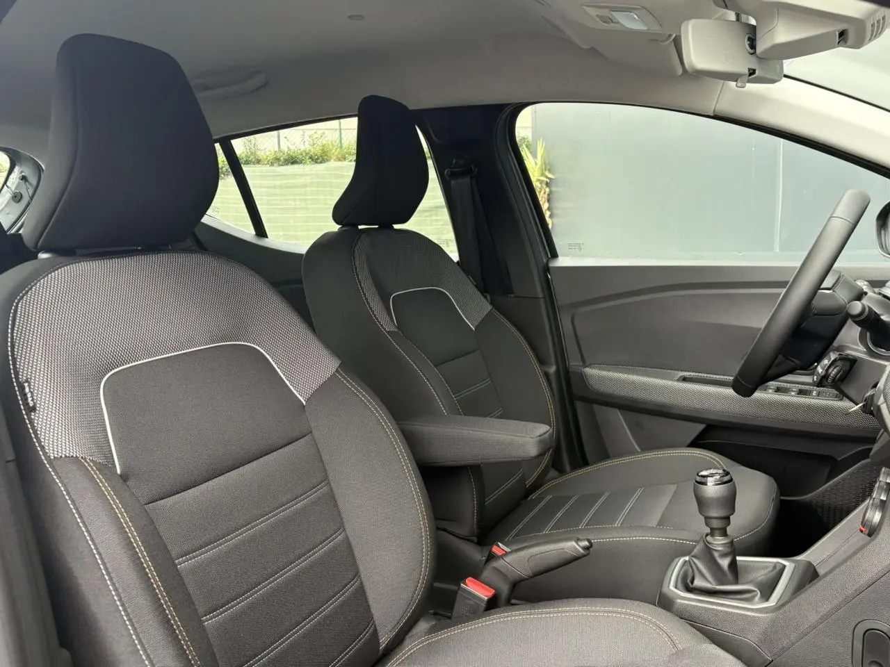 Vue intérieure côté droit du Dacia Sandero Stepway 2025, sièges noirs avec surpiqûres jaunes et accoudoir central.