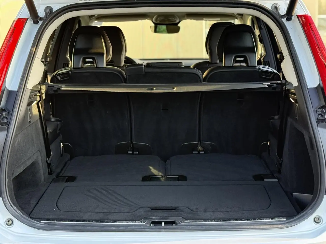 Coffre ouvert vu de l'arrière d'un Volvo XC90 blanc Crystal, montrant les sièges rabattus et l'intérieur noir.
