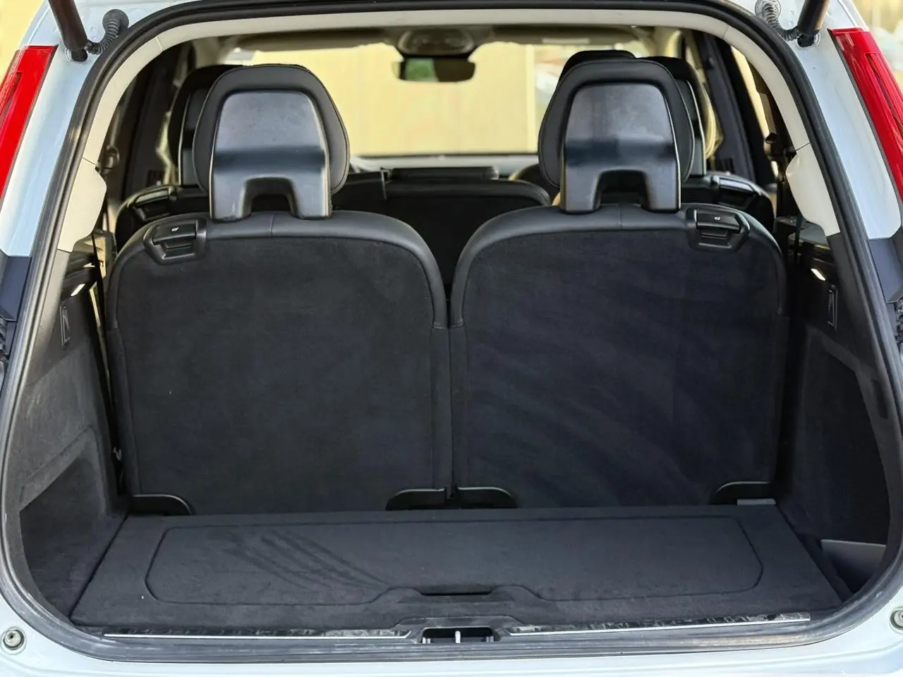 Coffre ouvert vu de l'arrière du Volvo XC90 blanc Crystal, montrant la troisième rangée de sièges noirs relevés.