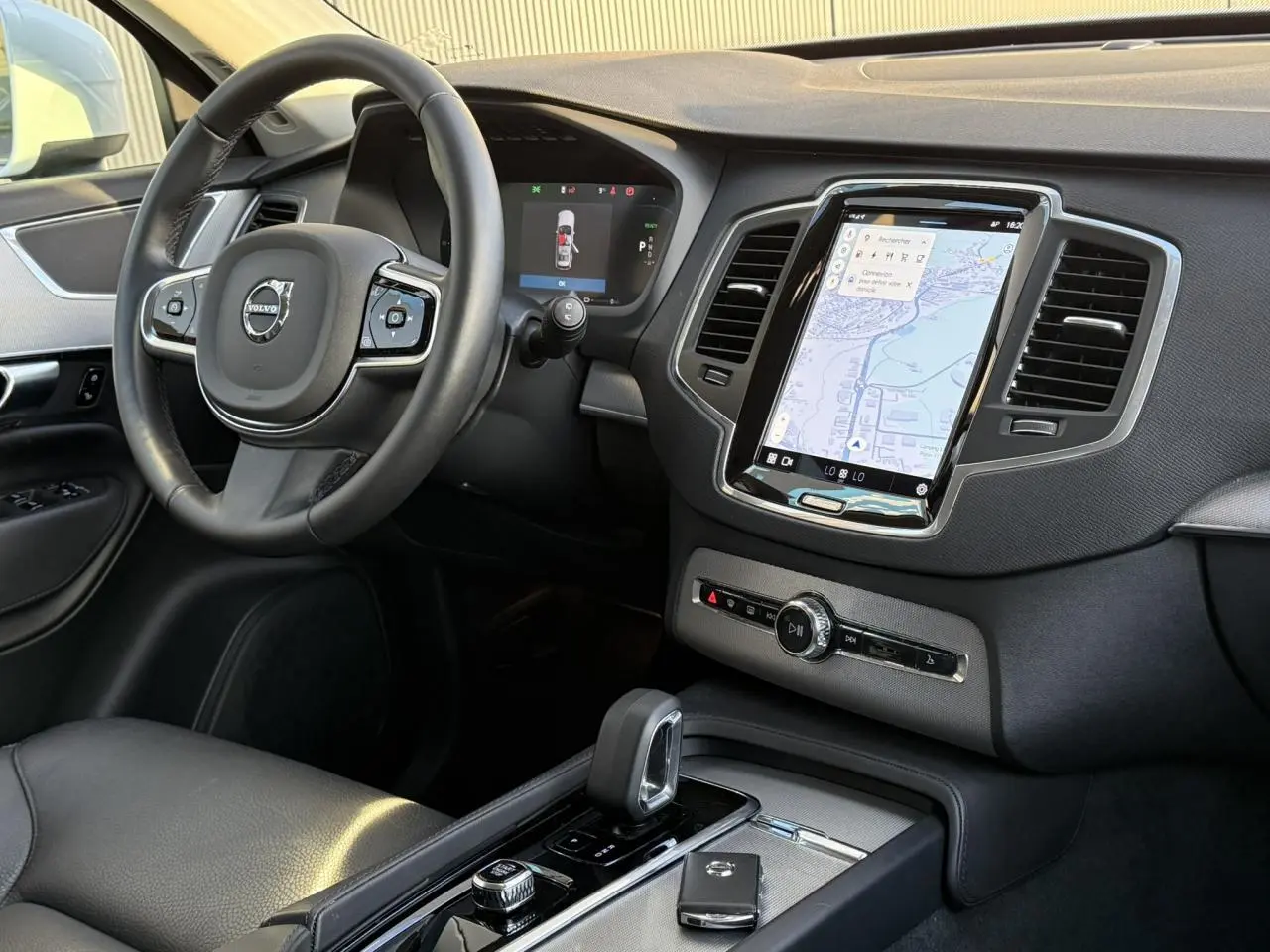 Vue intérieure côté conducteur du tableau de bord et console centrale du Volvo XC90 2024 avec écran tactile vertical et volant cuir noir.
