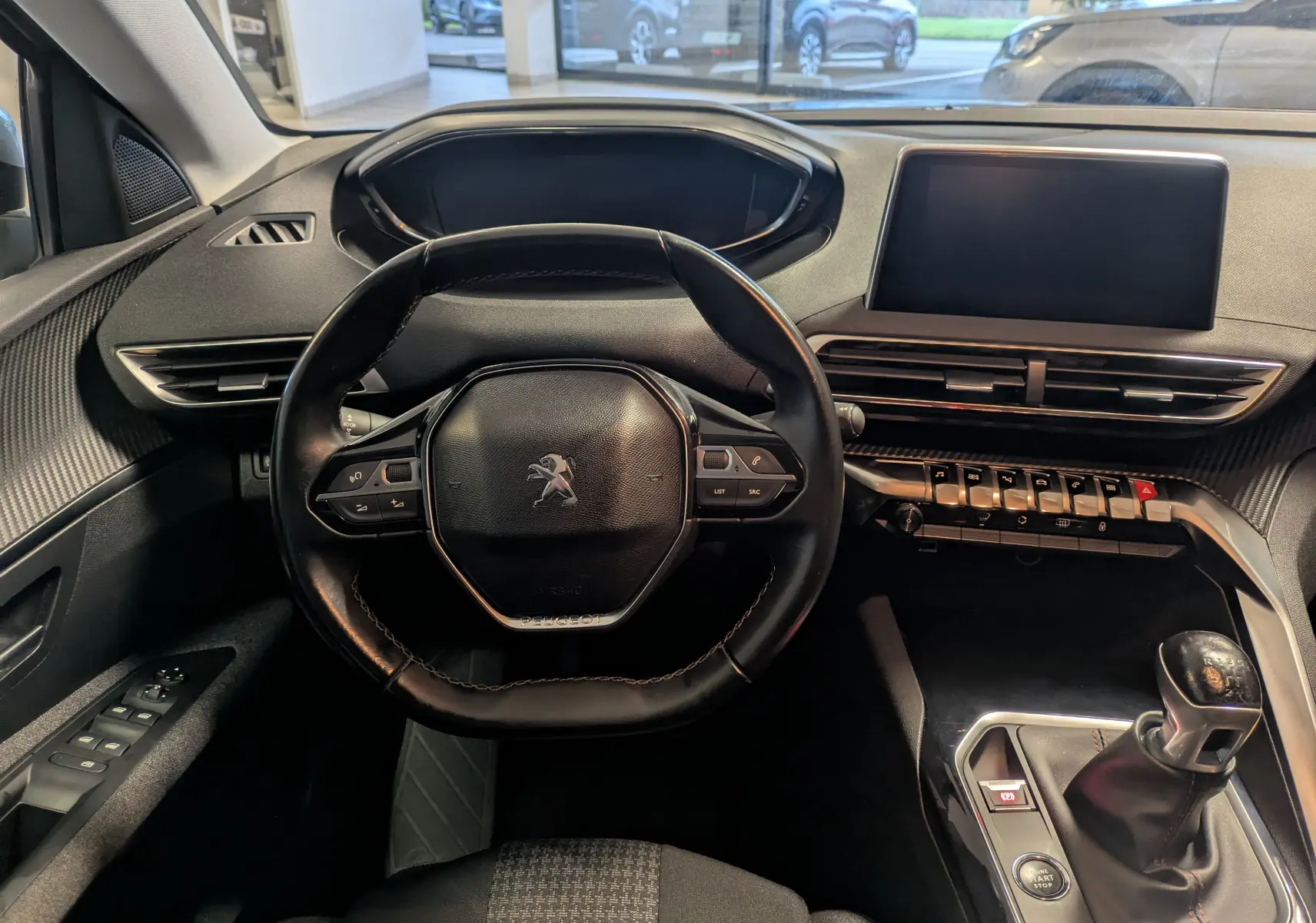 Vue intérieure centrée sur le volant et la console centrale d'un Peugeot 3008 gris Arthense avec boîte manuelle.