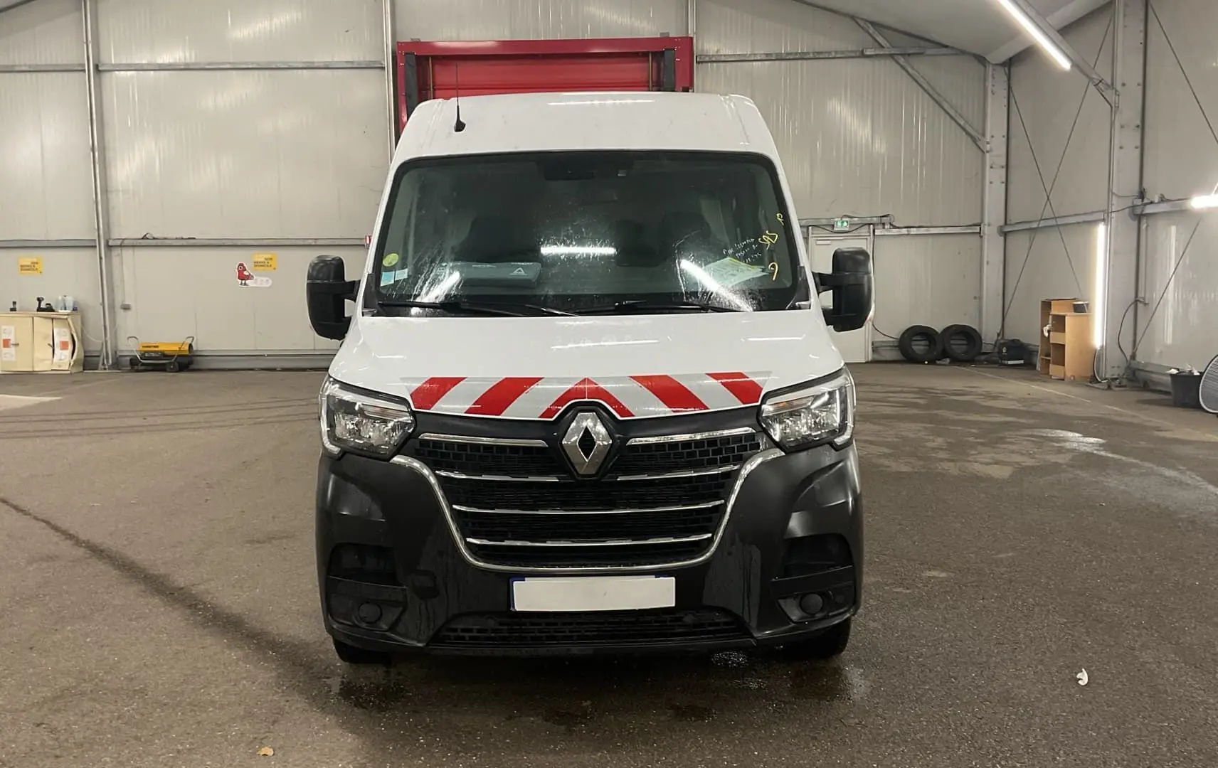 Vue avant d’un Renault Master cabine approfondie blanc avec marquage rouge et noir sur le pare-chocs dans un garage.