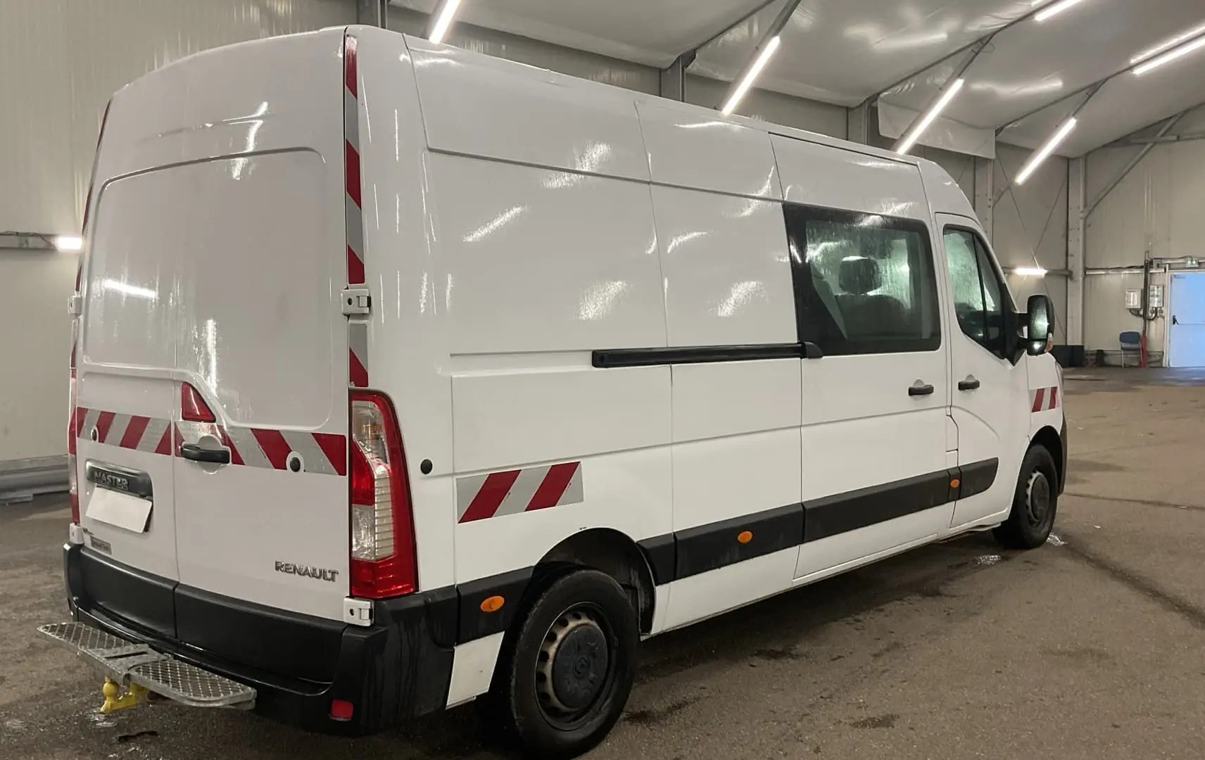 Vue 3/4 arrière droite d’un Renault Master blanc avec marquages réfléchissants rouges et blancs dans un garage.
