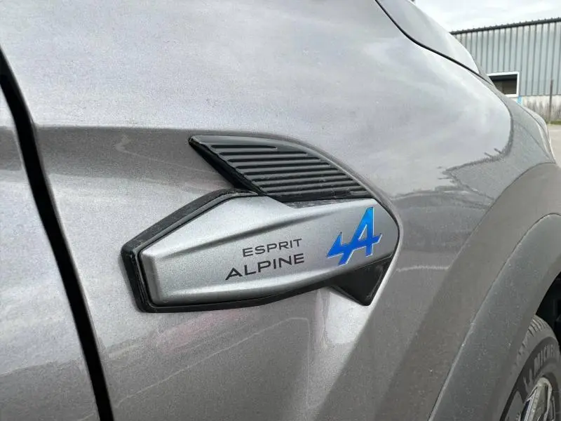 Gros plan sur l'emblème Esprit Alpine bleu sur la carrosserie gris Cassiopée du côté avant droit du Renault Captur 2026.