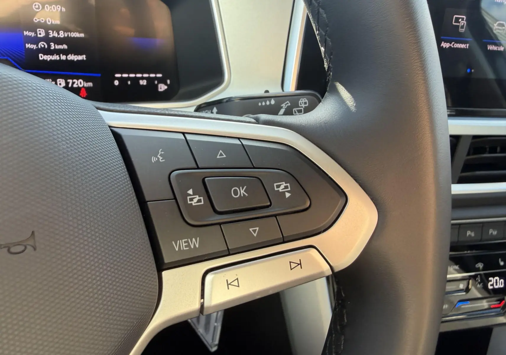Gros plan sur les commandes multifonctions gauche du volant cuir du Volkswagen T-Roc 2025, avec écran digital en arrière-plan.