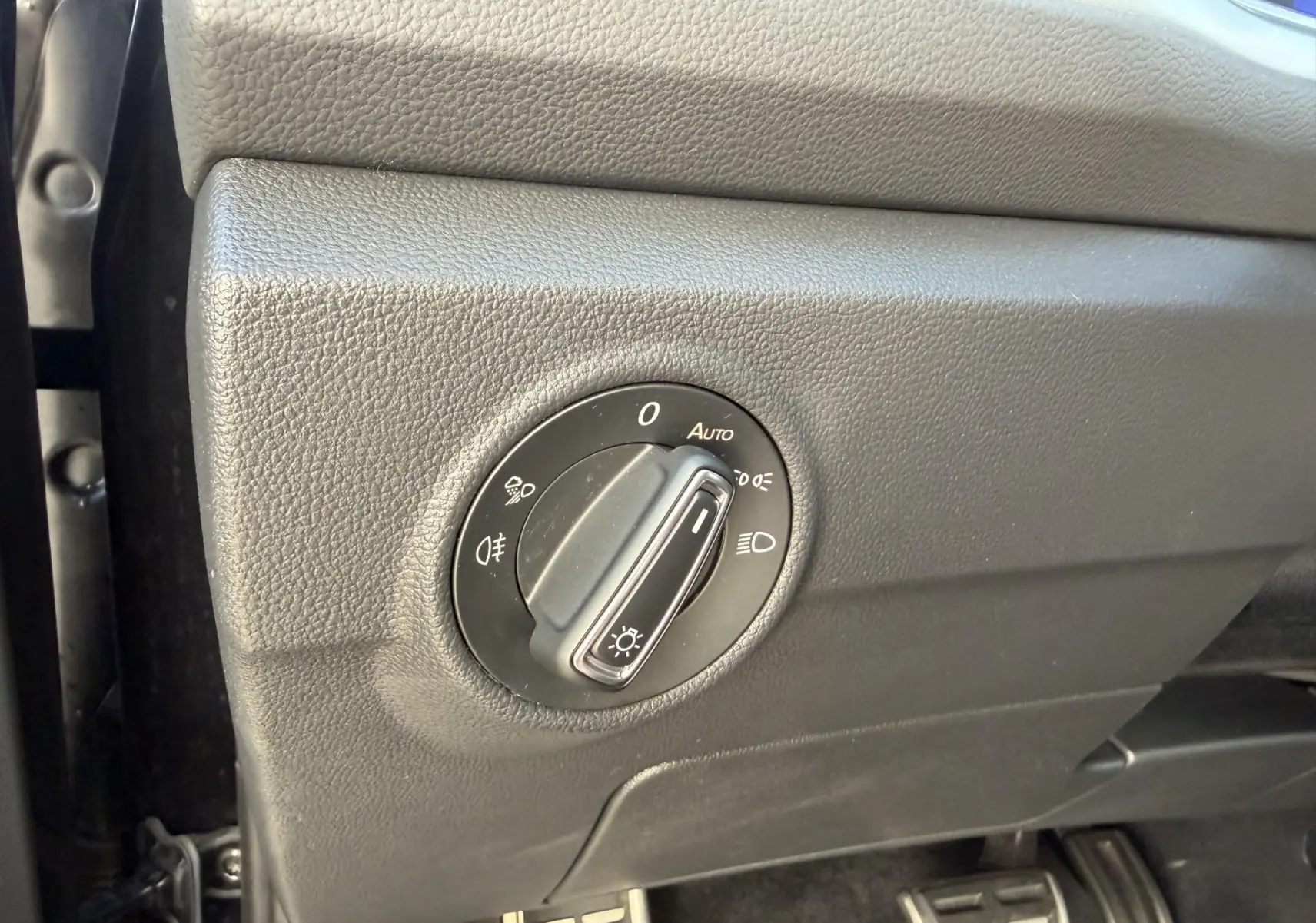 Gros plan sur le bouton de commande des phares dans l’habitacle noir du Volkswagen T-Roc 2025, côté conducteur.