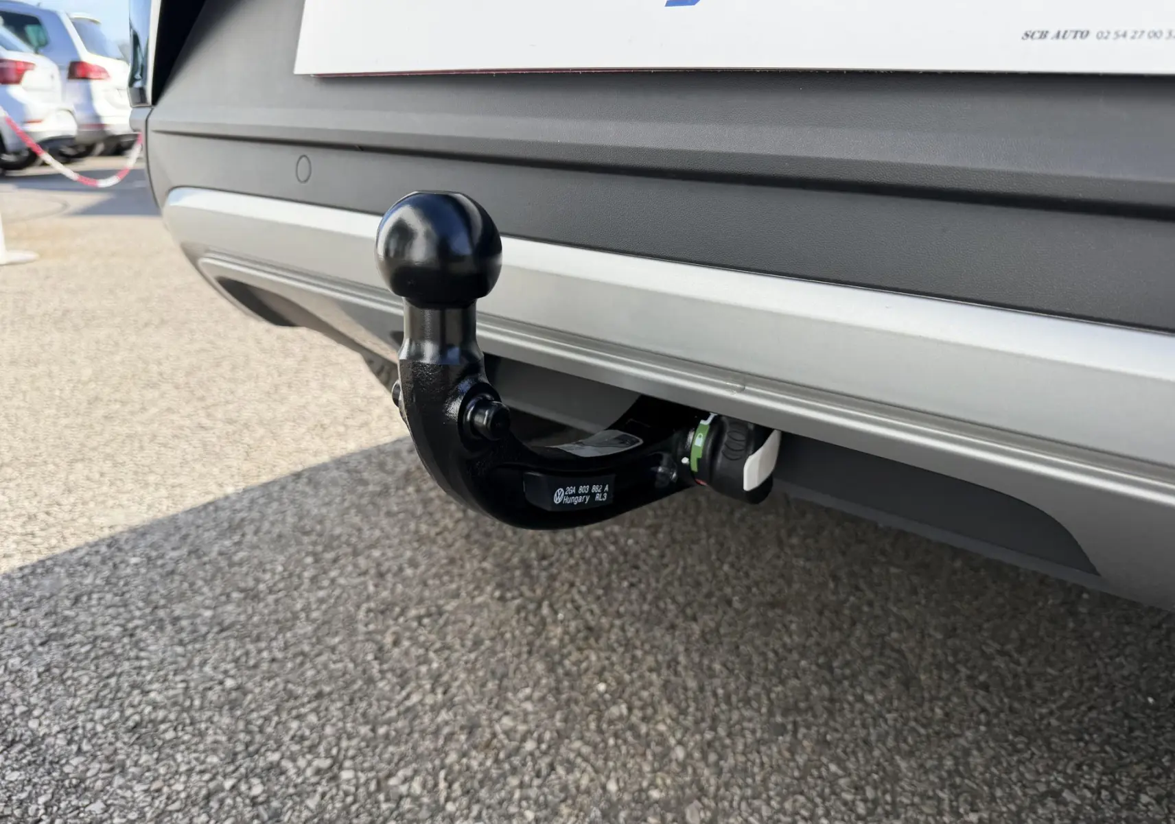 Gros plan sur l'attelage amovible noir fixé à l'arrière d'un Volkswagen T-Roc noir, sur fond de parking asphalté.