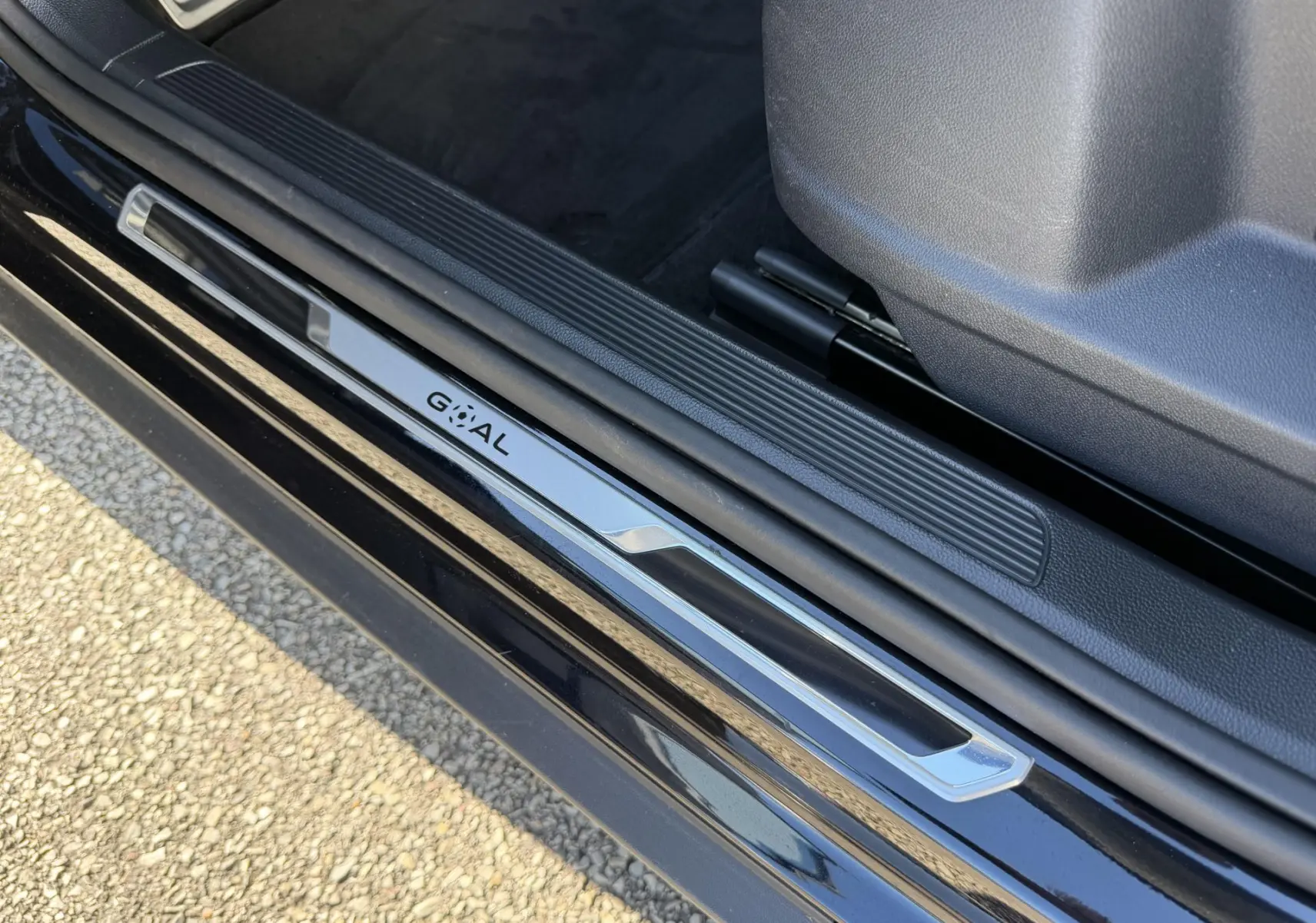 Gros plan sur la partie basse de la porte côté conducteur d'un Volkswagen T-Roc noir avec seuil de porte "GOAL" chromé.