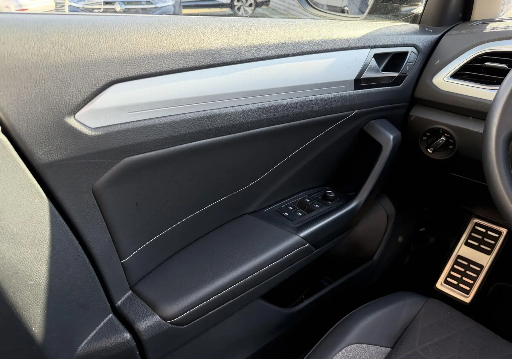 Vue intérieure côté conducteur du Volkswagen T-Roc 2025, montrant la portière noire avec commandes électriques et surpiqûres blanches.