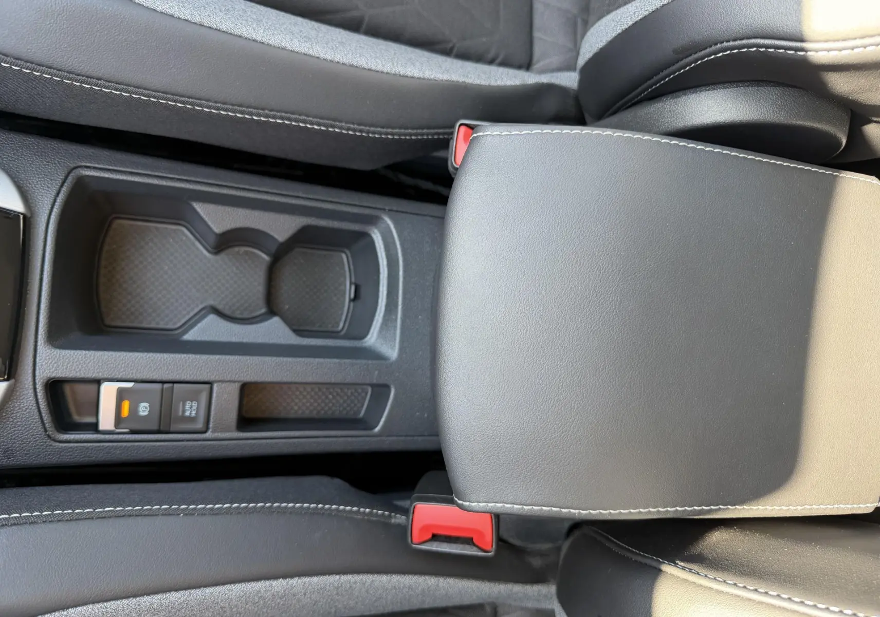 Vue rapprochée de la console centrale noire du Volkswagen T-Roc 2025, avec accoudoir et porte-gobelets.