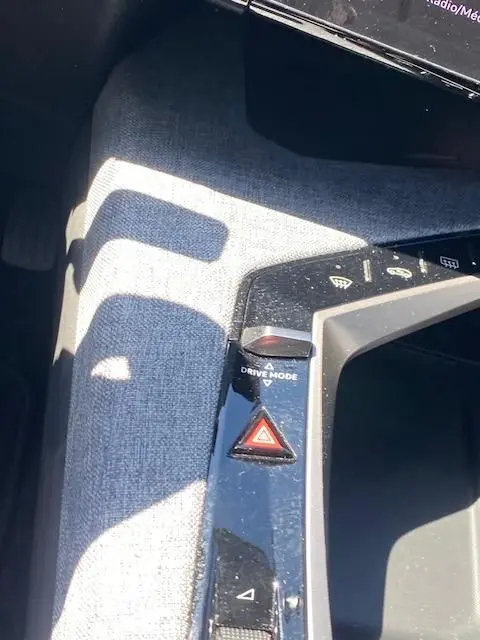 Gros plan sur la console centrale du Peugeot 3008 noir, montrant le bouton Drive Mode et la commande des feux de détresse.