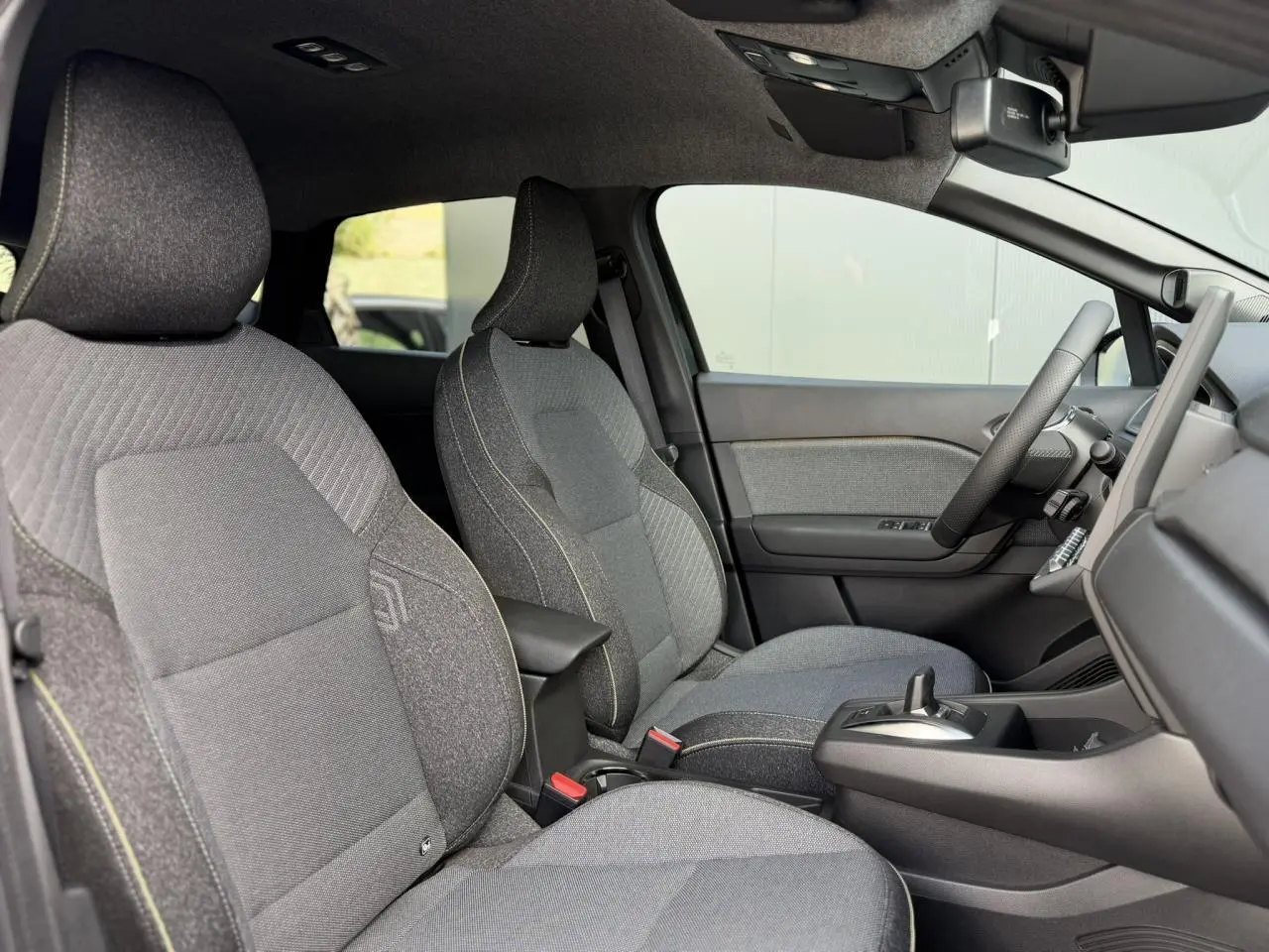 Vue intérieure côté droit du Renault Captur 2026, sièges gris tissu avec surpiqûres jaunes et console centrale noire.