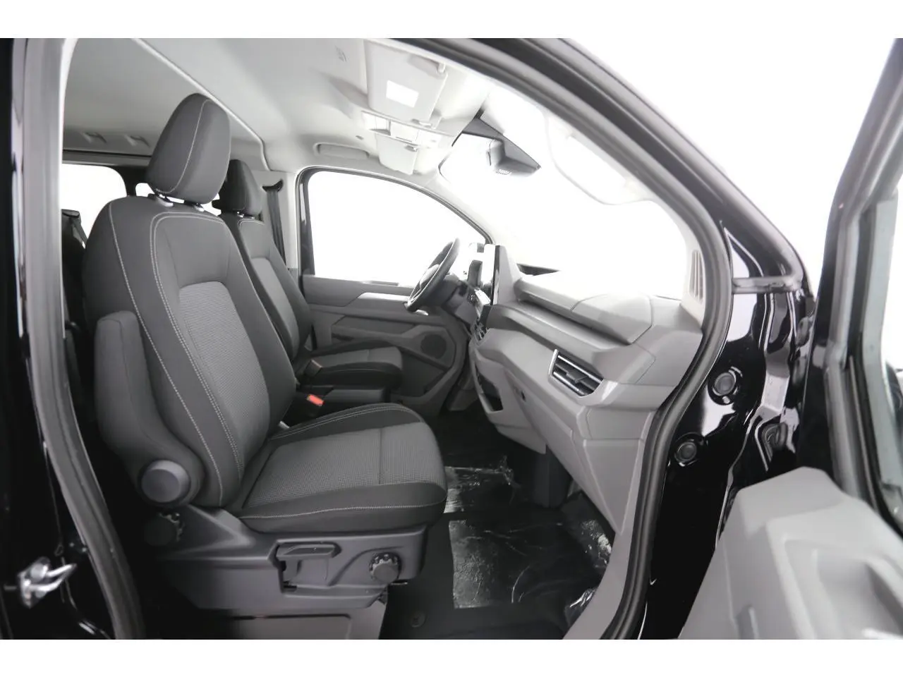 Vue intérieure côté conducteur du Volkswagen Transporter T7 ProCab 2025, sièges tissu gris et tableau de bord moderne.