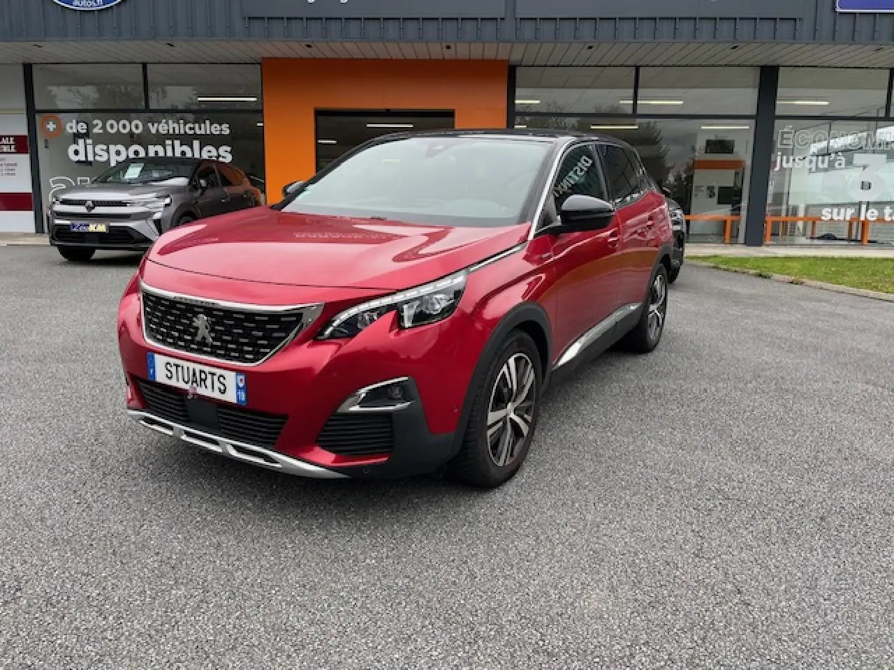 Peugeot 3008 GT Line rouge Ultimate vue 3/4 avant droit avec toit noir et jantes alliage bi-ton devant un showroom.