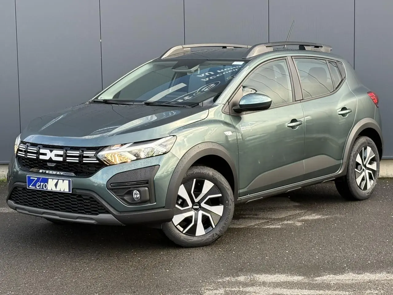 Dacia Sandero Stepway TCE 90 vert cèdre en 3/4 avant droit avec barres de toit et jantes spécifiques.