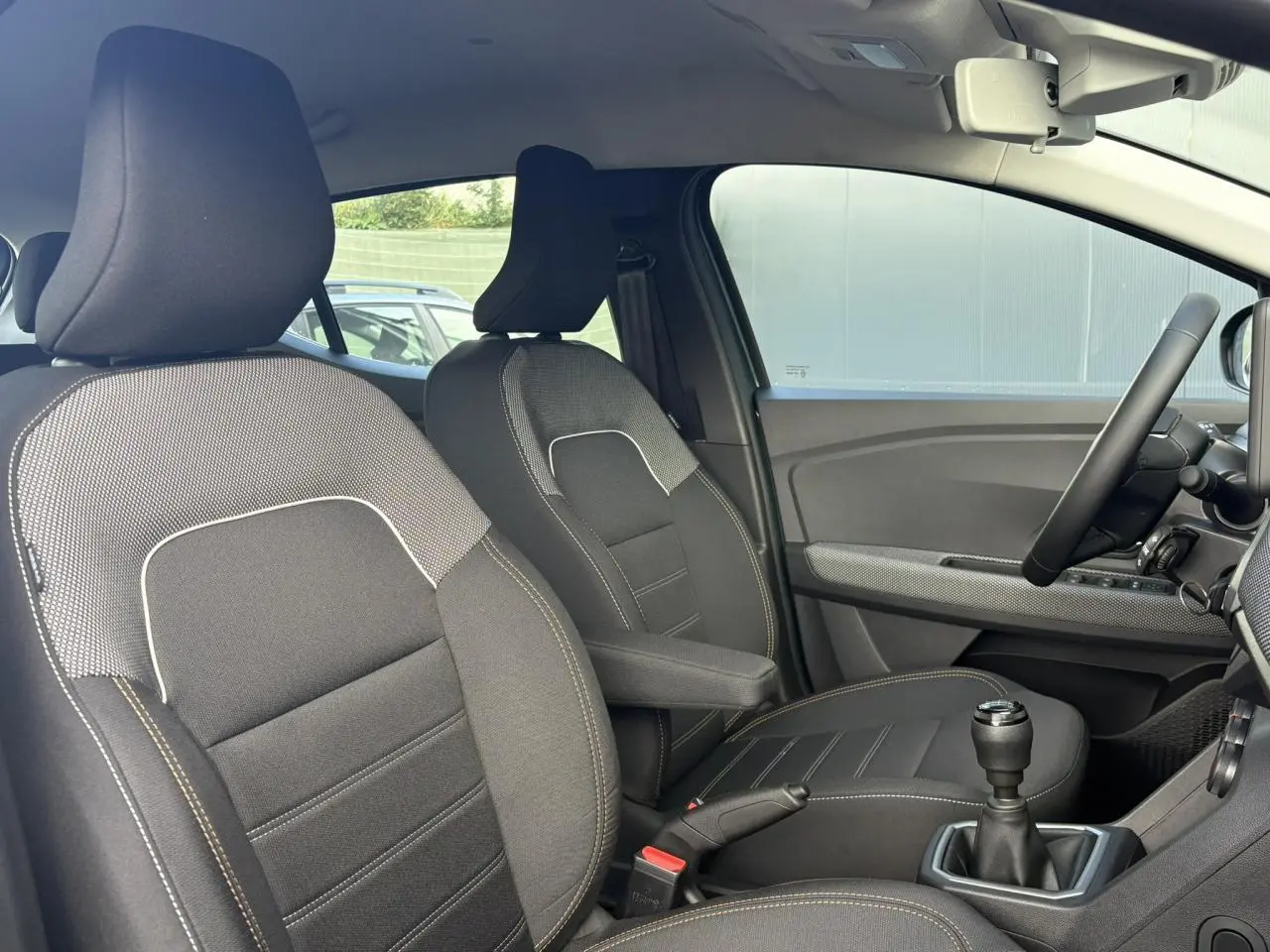 Vue intérieure côté conducteur de la Dacia Sandero Stepway 2025, sièges noirs avec accoudoir central et volant Soft Feel.