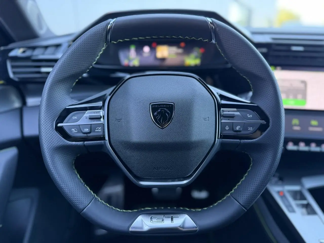 Gros plan sur le volant cuir perforé noir avec surpiqûres vertes et logo GT du Peugeot 408 Hybrid 2025.
