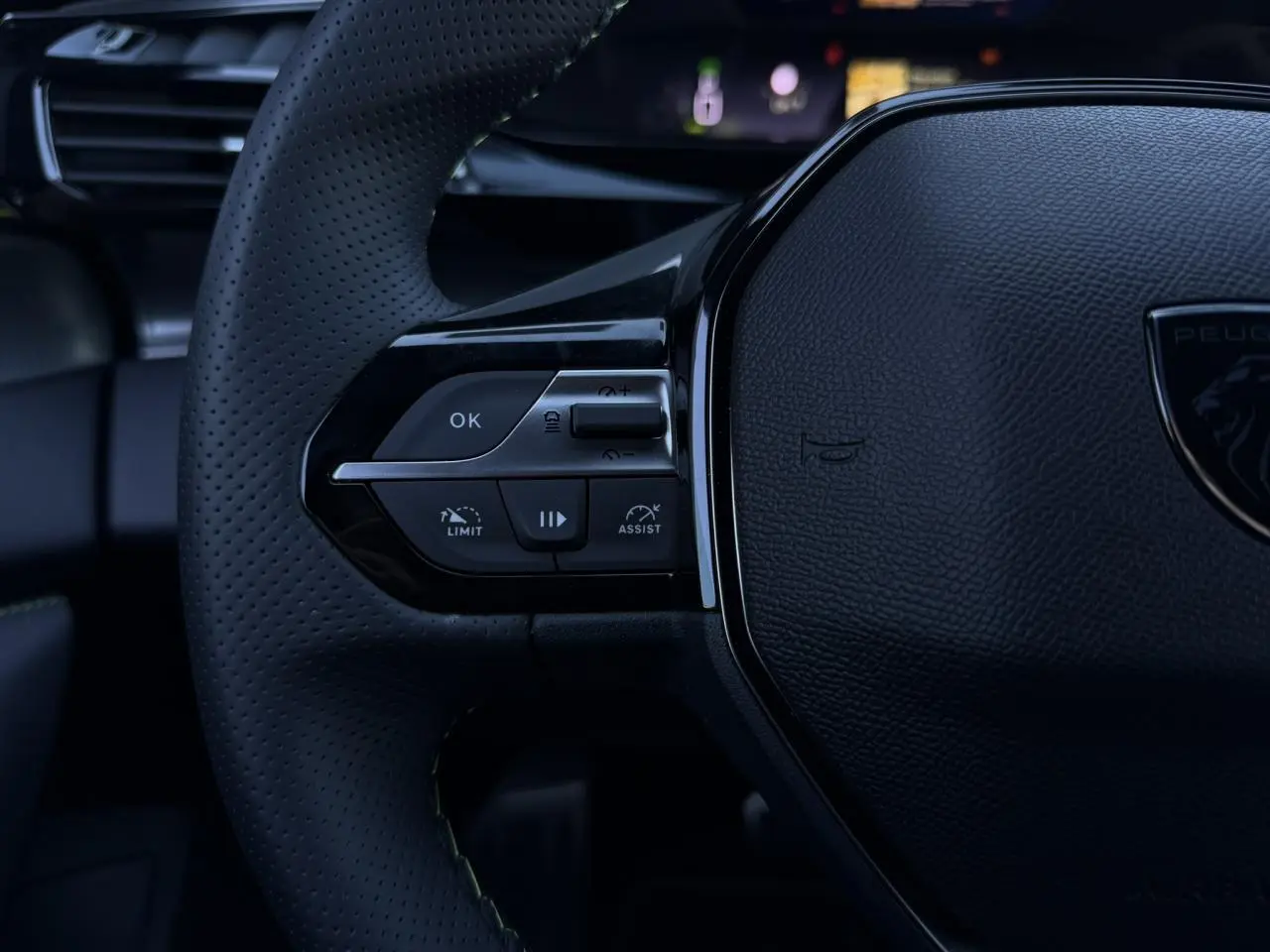 Gros plan sur le volant perforé noir de la Peugeot 408 Hybrid 145 e-DSC6 GT avec commandes intégrées côté gauche.
