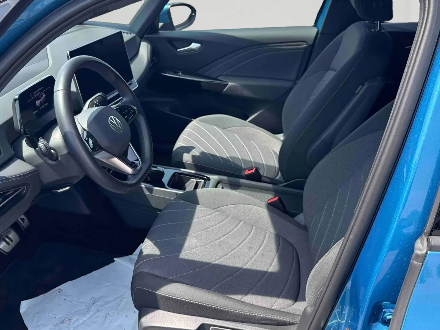 Vue intérieure côté conducteur du Volkswagen ID.3 bleu, montrant sièges gris et tableau de bord digital.