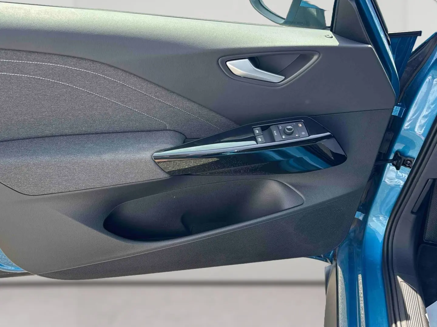 Vue rapprochée de la porte avant gauche bleu métallisé du Volkswagen ID.3 avec commandes électriques et garniture tissu grise.