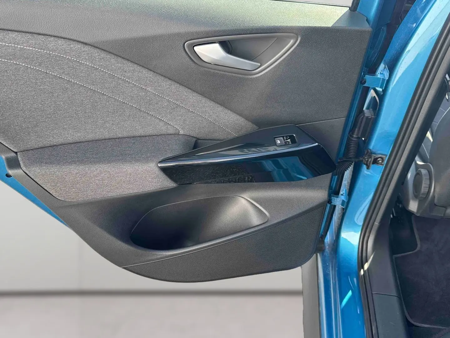 Vue rapprochée de la porte avant gauche bleu métallisé du Volkswagen ID.3 avec garniture noire et commandes de fenêtre.