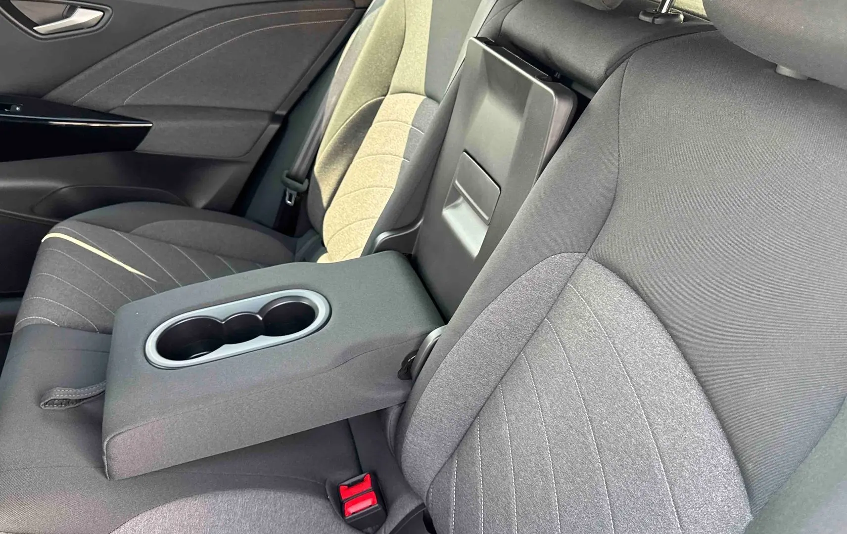 Vue intérieure côté droit des sièges arrière gris avec accoudoir central relevé et porte-gobelets du Volkswagen ID.3 2025.
