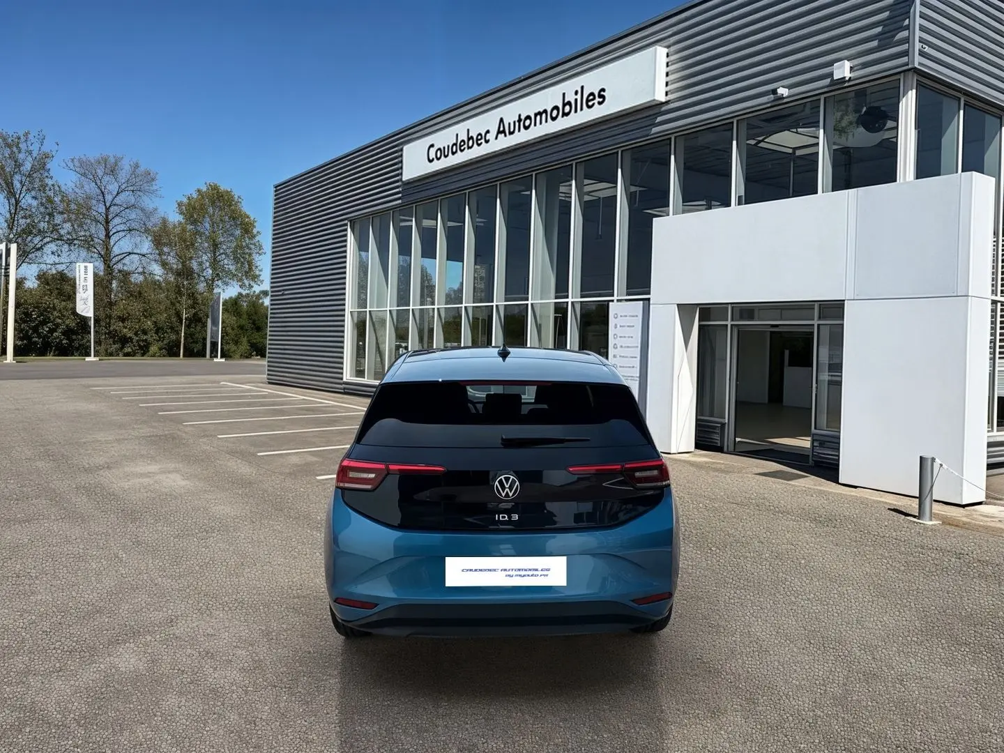Vue arrière d'une Volkswagen ID.3 bleue métallisée avec toit noir, stationnée devant un bâtiment Coudebec Automobiles.