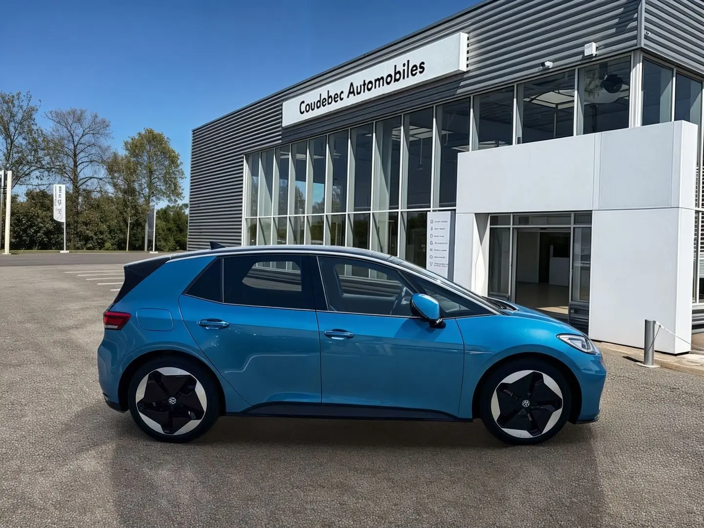 Profil côté gauche d'un Volkswagen ID.3 204 ch Pro S 77 kWh bleu métallisé avec toit noir, stationné devant un bâtiment.