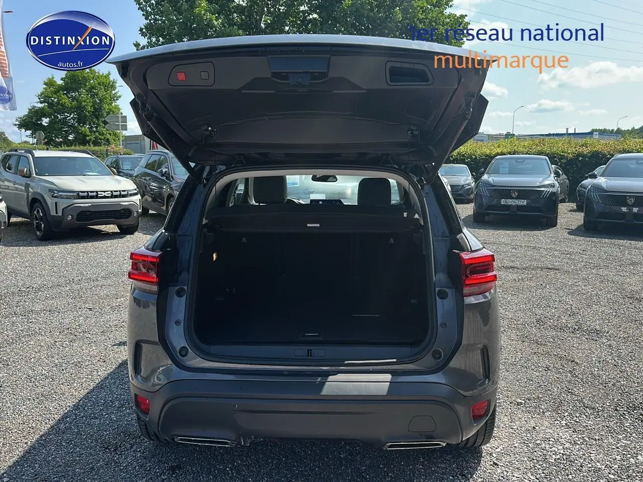 Vue arrière d'un Citroën C5 Aircross gris platinium 2024 avec hayon ouvert et coffre visible sur parking.