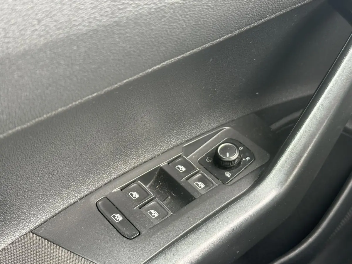 Gros plan sur les commandes de lève-vitres et réglage des rétroviseurs côté conducteur d'une Volkswagen Polo bleu 2021.