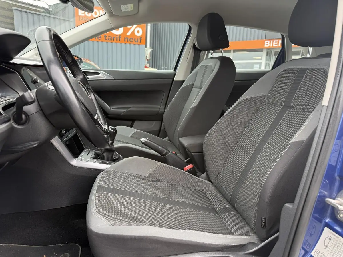 Intérieur avant de la Volkswagen Polo bleu 2021, sièges sport tissu gris avec volant et levier de vitesse manuels visibles.